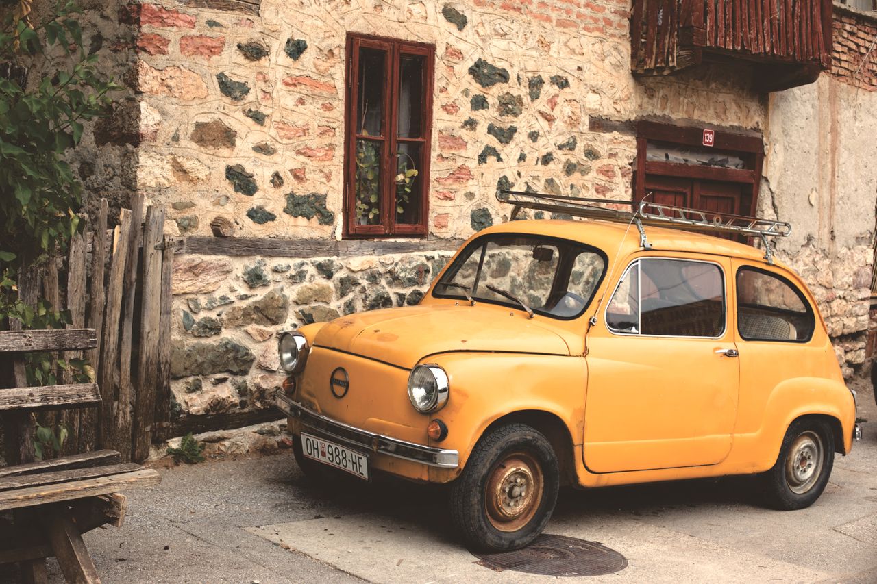 old yellow car parked by a rustic stone building embracing vintage cha