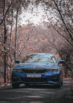 Stunning blue luxury car driving through a picturesque leaf-lined road during autumn.