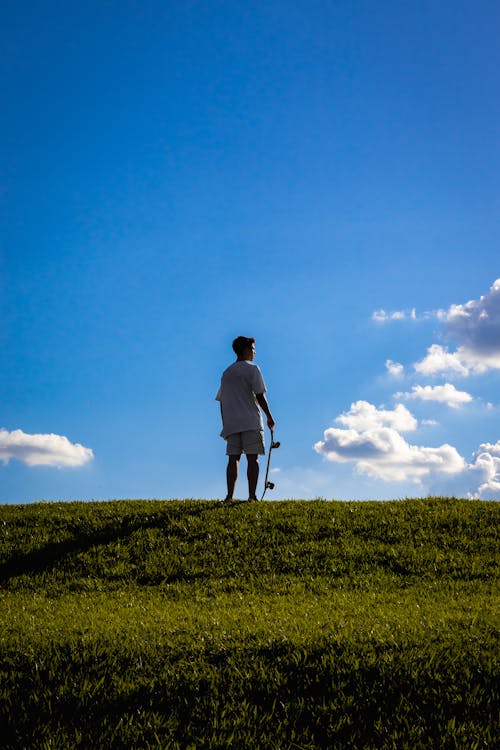 Free A Man Standing on Green Grass Holding a Skateboard Stock Photo