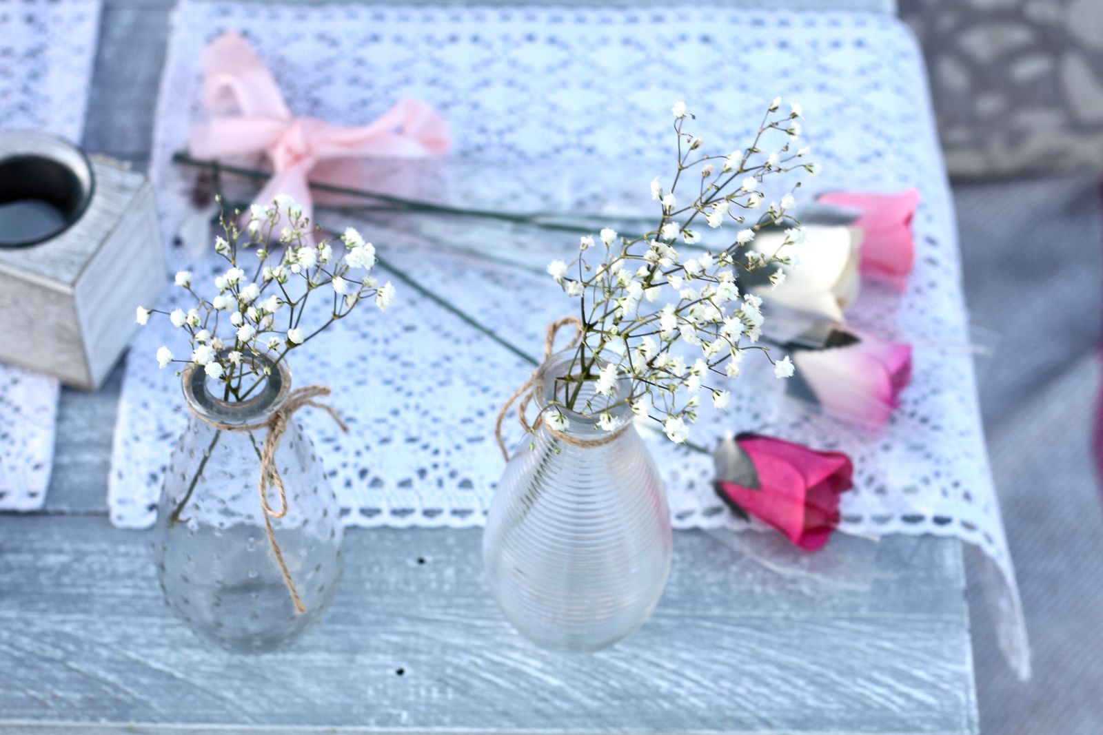 Delicate white baby's breath in glass vases on a lace-topped table with pink roses.