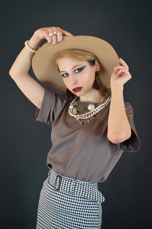 Stylish young female model adjusting hat in black studio