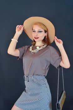 Smiling female wearing elegant skirt and blouse adjusting hat and looking away against blue background
