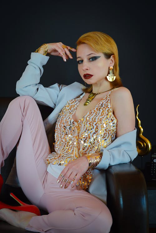 Confident female model wearing fashionable clothes sitting on couch and touching head while looking at camera
