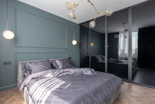 Interior design of bedroom with comfortable bed covered with gray blanket placed near mirrored cupboard