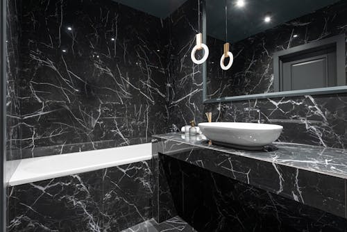 Contemporary interior design of bathroom with marble gray till on walls and stylish lamp reflecting in mirror above sink