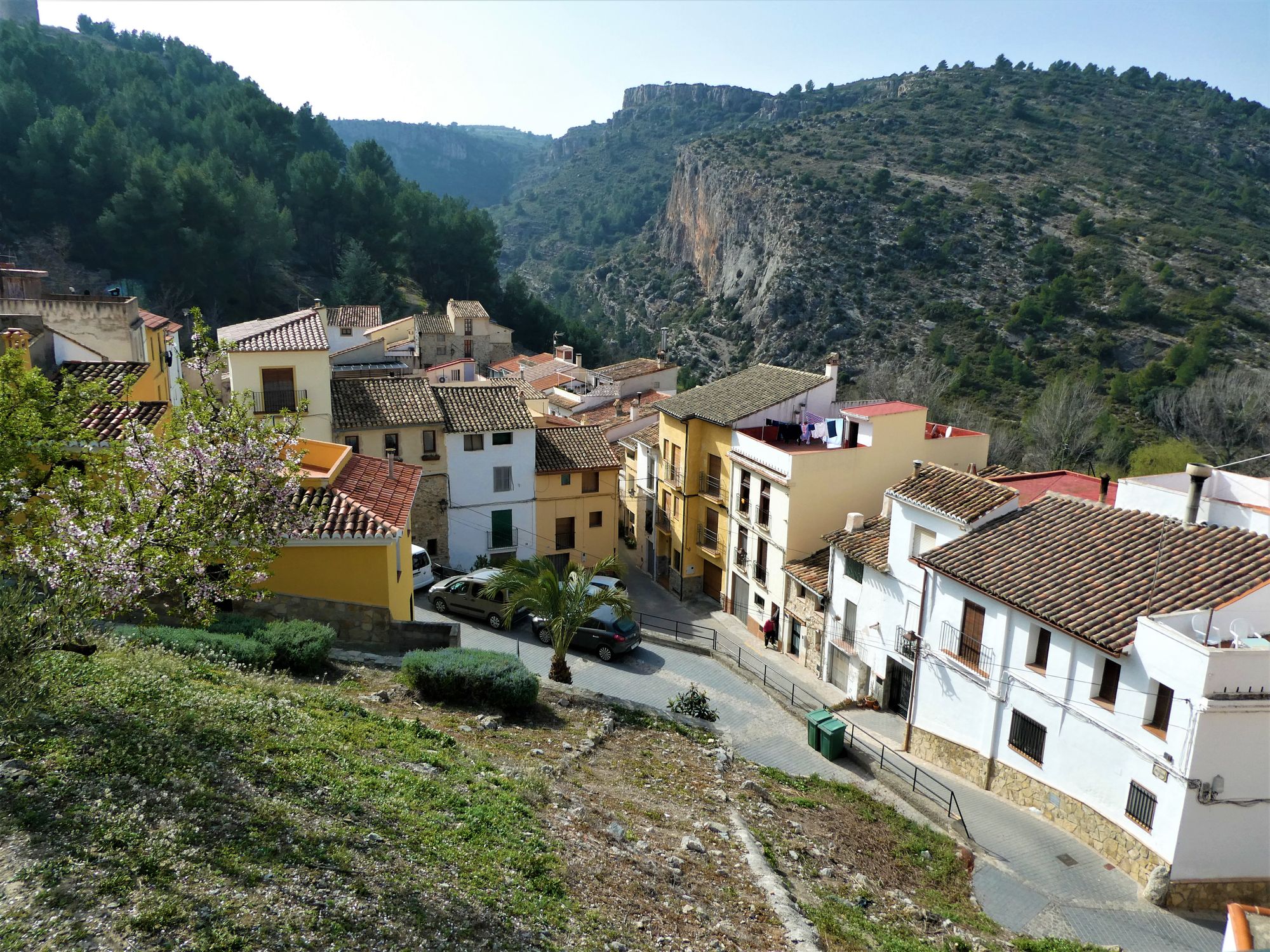 Carretera estrecha de montaña que sube hacia un pueblo de piedra entre vegetación seca