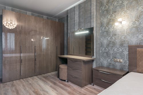 Interior of room with glossy cupboard with chest of drawers with mirror and nightstand near bed