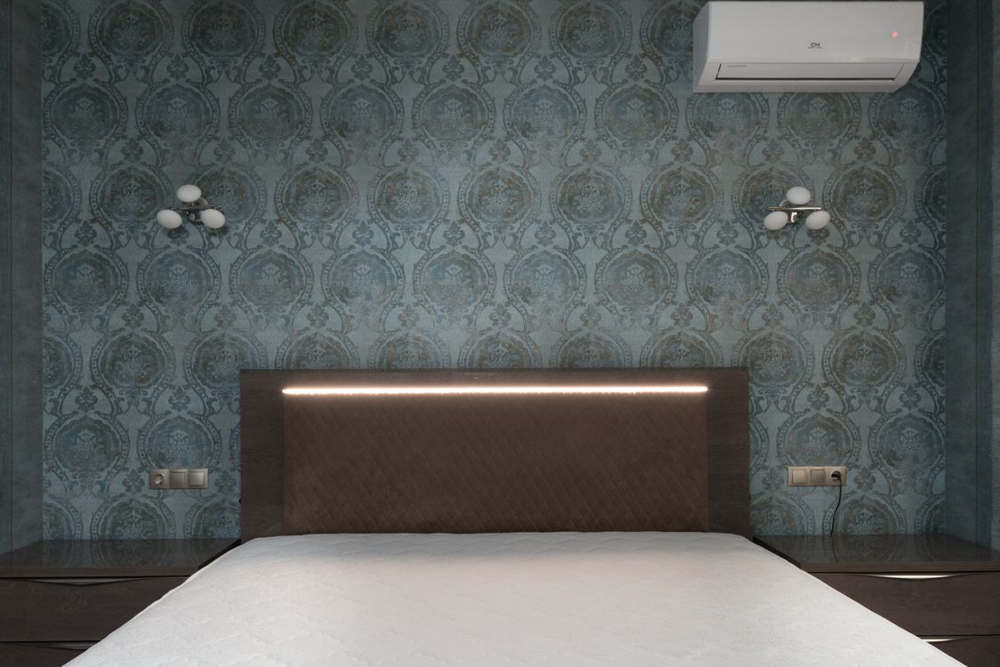 Free White mattress on bed with brown headboard placed between bedside tables at wall with ornamental wallpaper and decorative white sconces carpet head Stock Photo