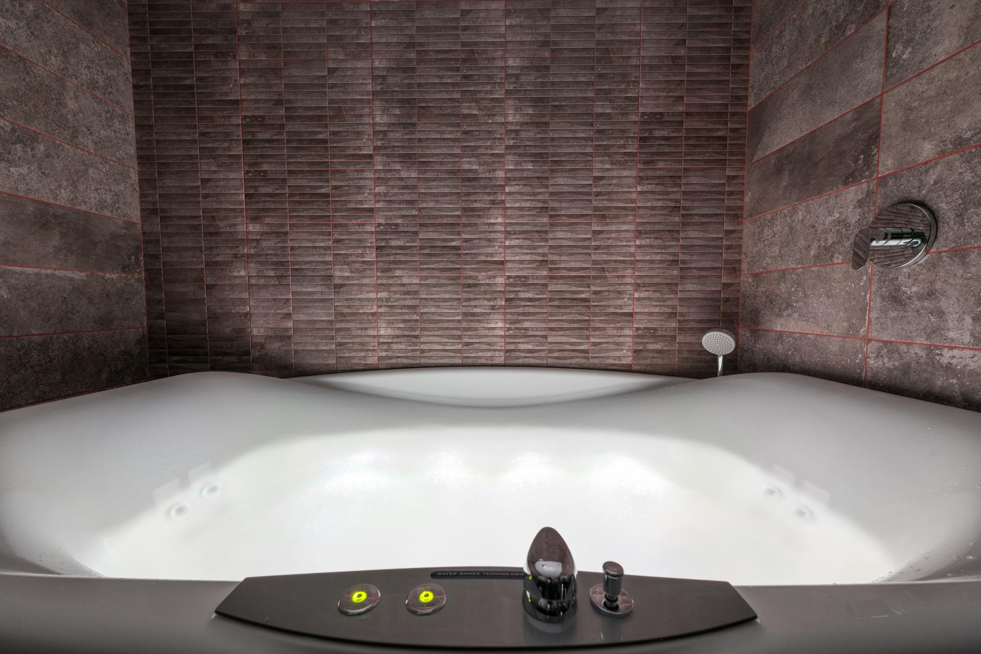 Modern white ceramic tub with illumination and contemporary control panel with buttons and levers placed in stylish bathroom among walls