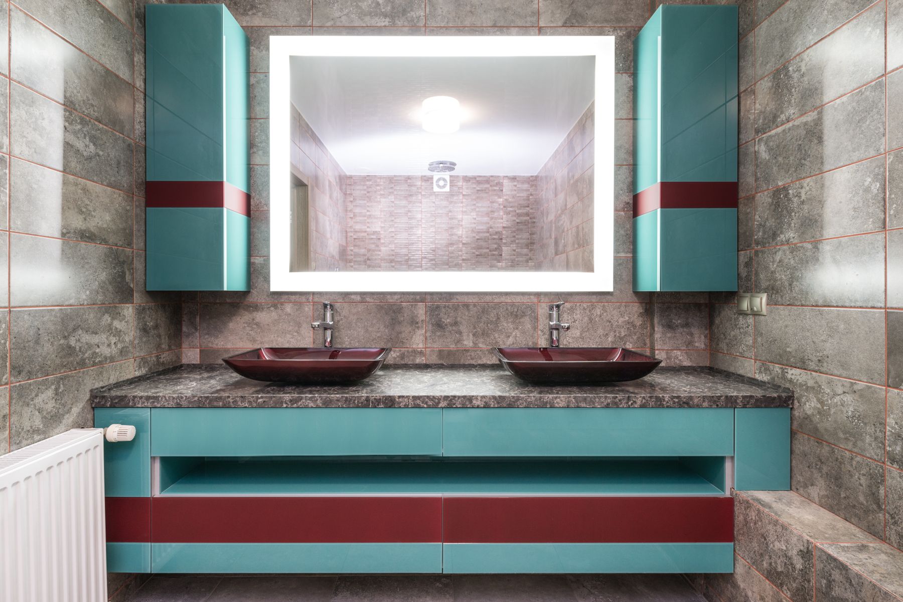 Bathroom with turquoise cabinets, colored sinks and illuminated mirror