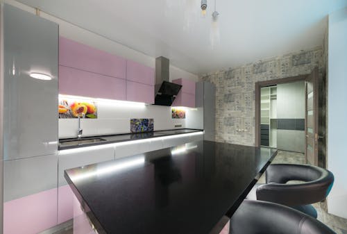 Black table with chairs placed near colorful cupboards and modern kitchenware in stylish kitchen with opened door in spacious apartment
