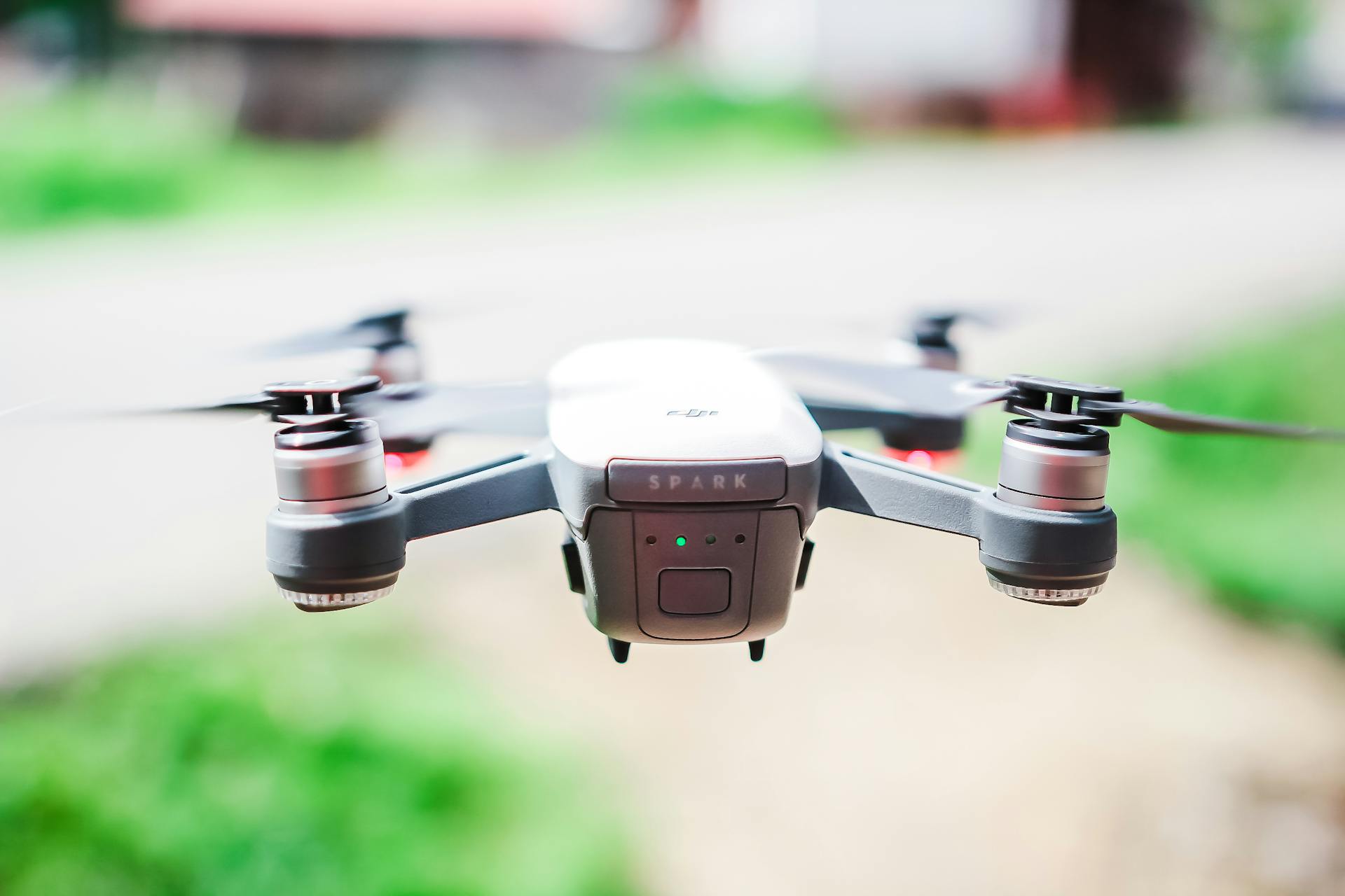 A front view of a DJI Spark drone flying in a blurred outdoor setting, capturing technology in motion.