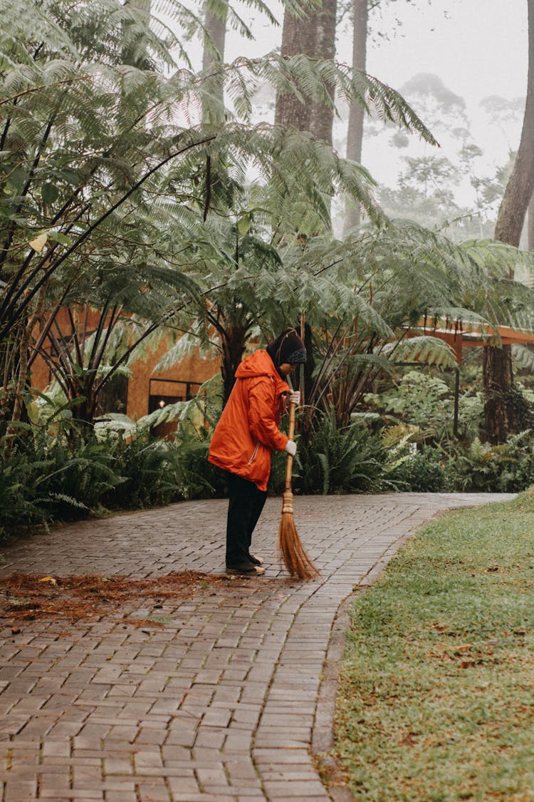 A Person In Orange Jacket Sweeping On The Street