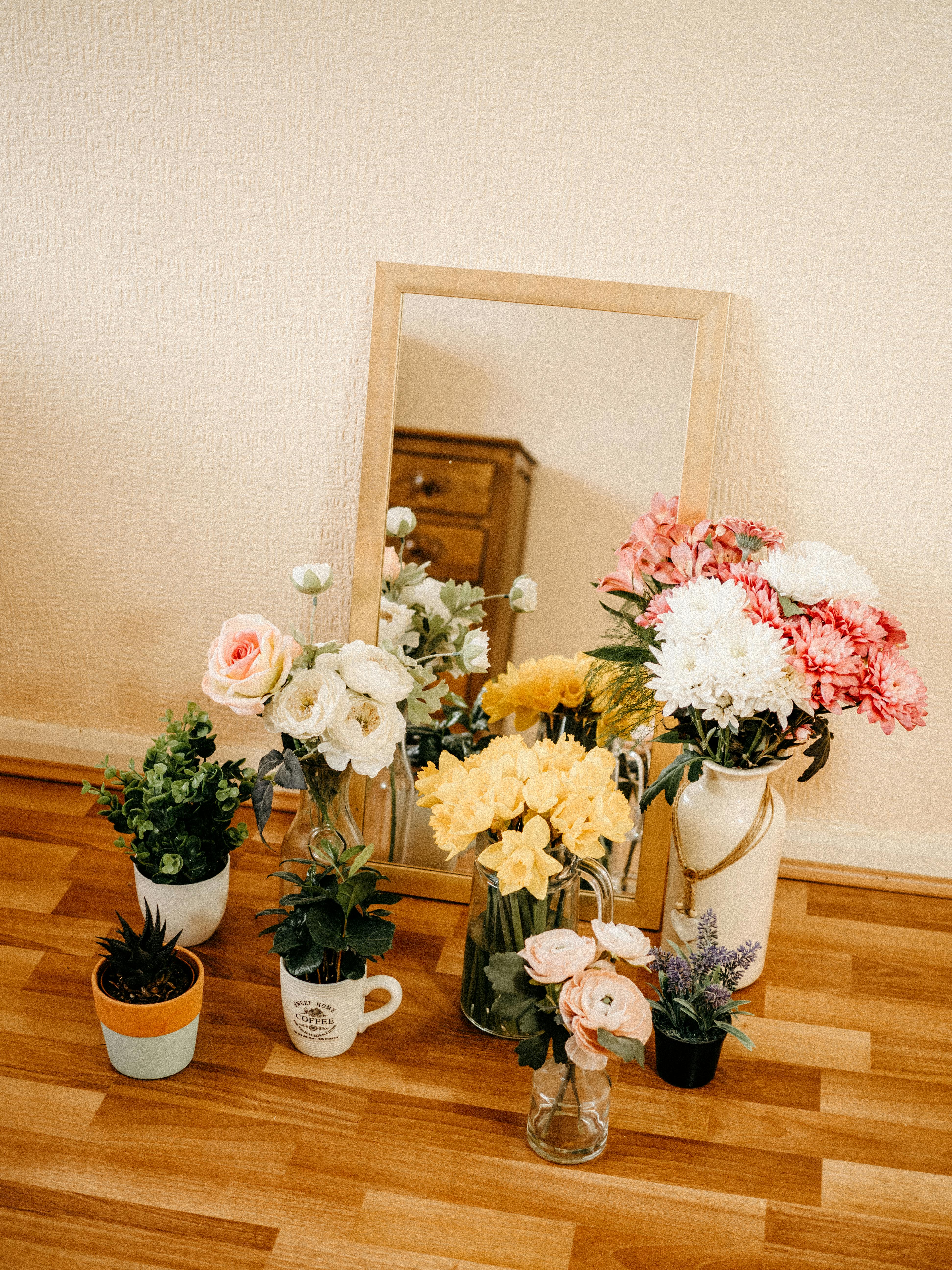 A beautiful indoor flower arrangement with various plants in front of a mirror.