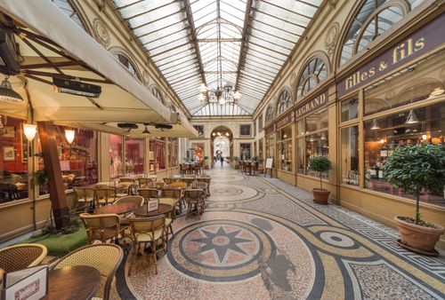 Free Discover the charm of Paris in a classic passage with ornate architecture, inviting café tables, and vintage shops. Stock Photo
