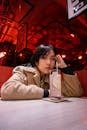 A Woman in Beige Coat Sitting Near the Table with Cocktail Drink