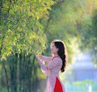 A Woman in Floral Dress Touching the Green Leaves of a Bamboo Tree
