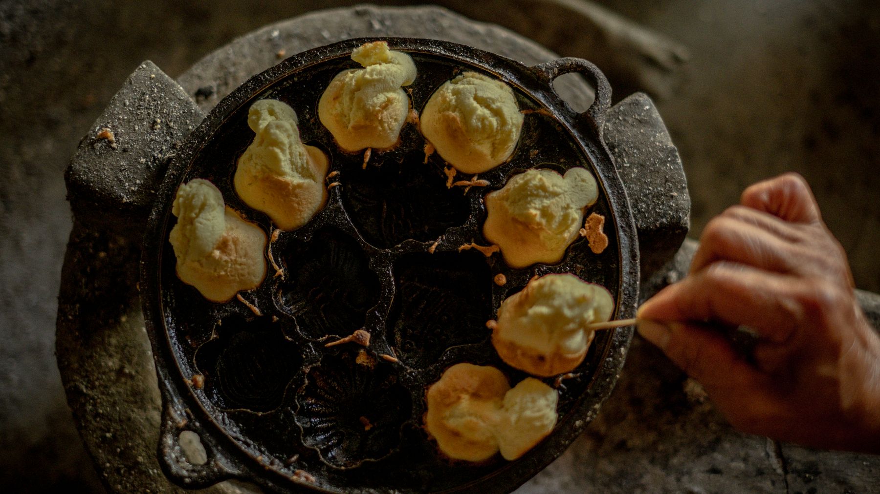 Close-up of hand cooking traditional Vietnamese cakes on a cast-iron pan.
