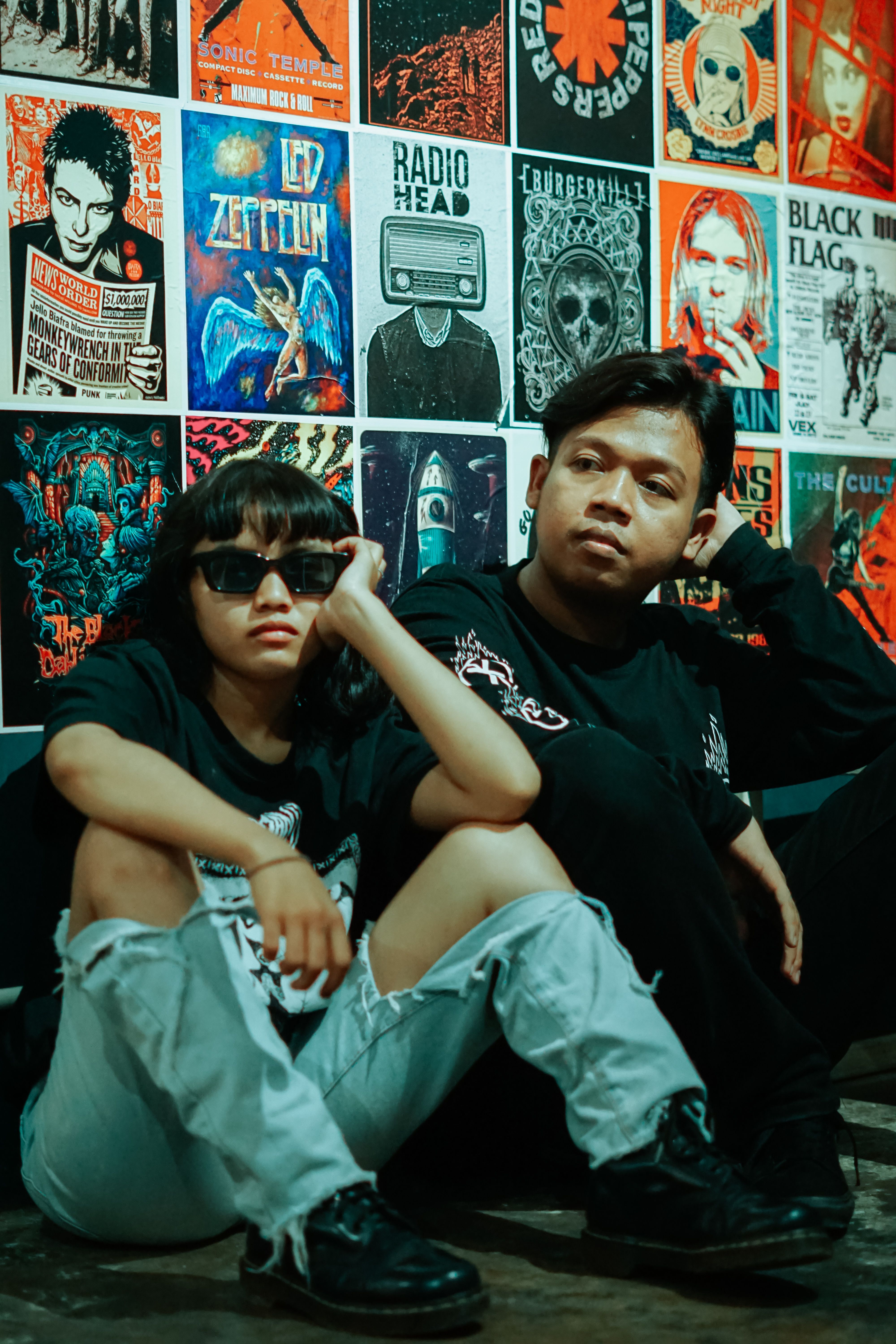 Casual portrait of two people against a rock music poster wall, exuding a relaxed urban vibe.