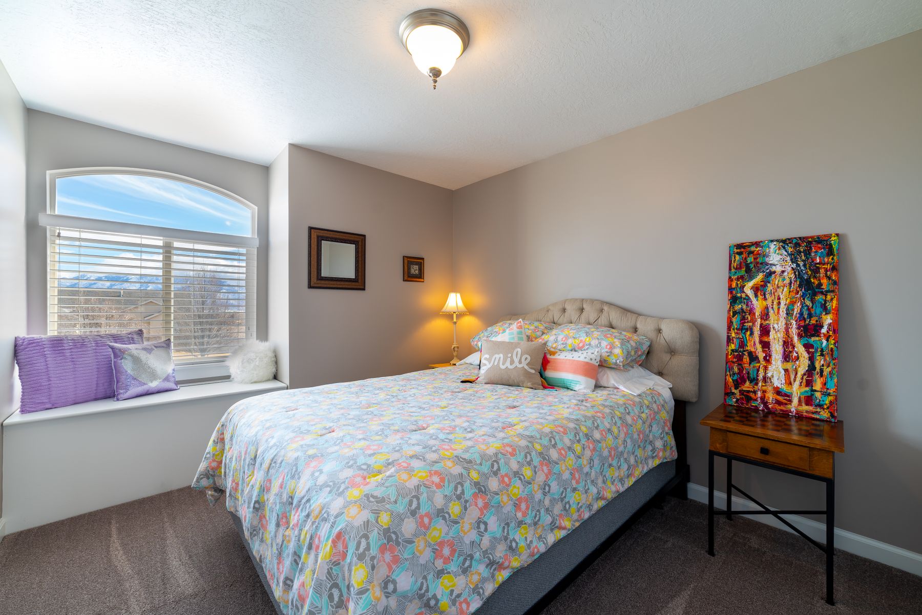 Bright bedroom with floral bedding, colorful cushions, vivid framed art and warm bedside lamps
