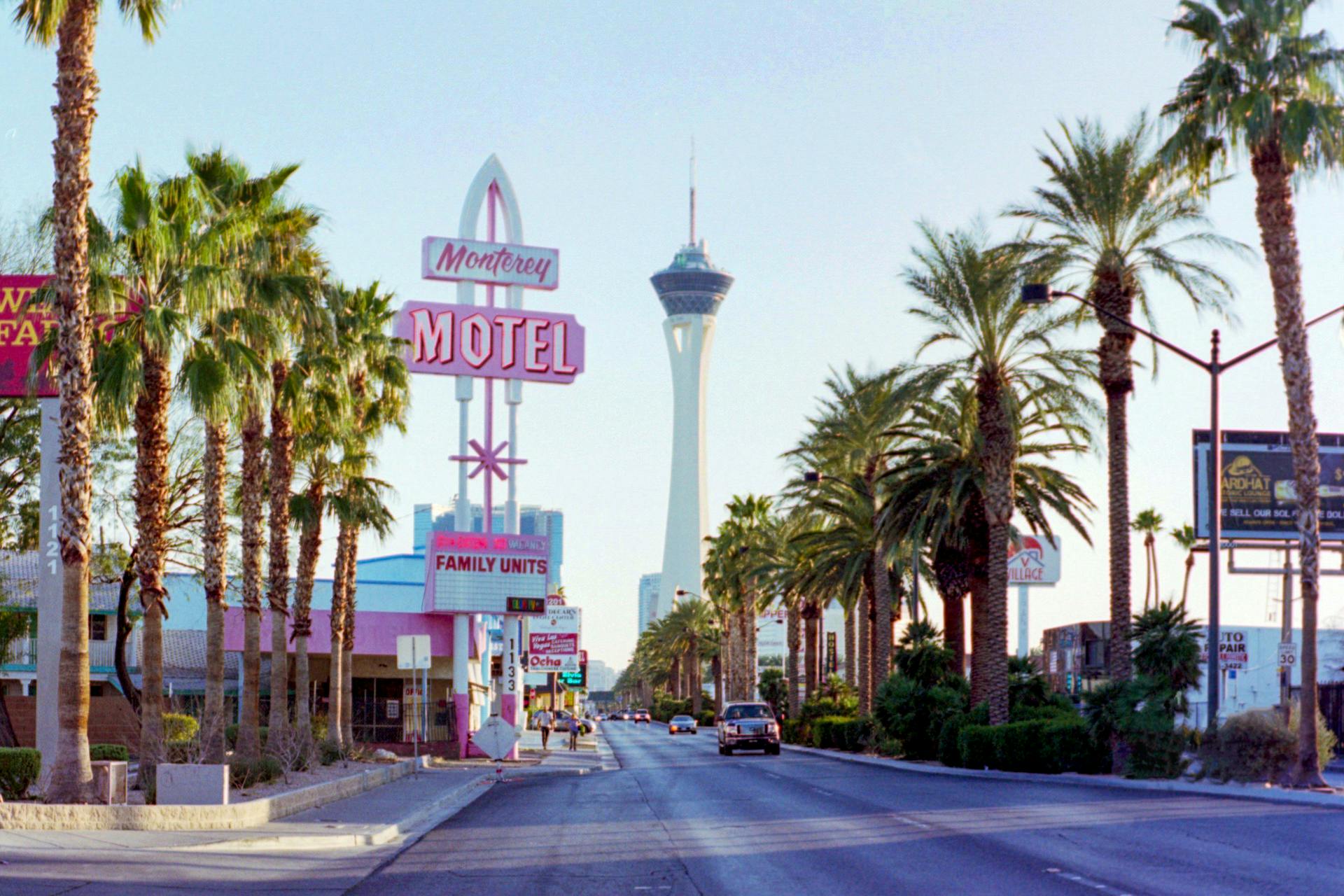 A street view of Las Vegas Boulevard showcasing the iconic Stratosphere Tower and a classic motel sign under clear skies.