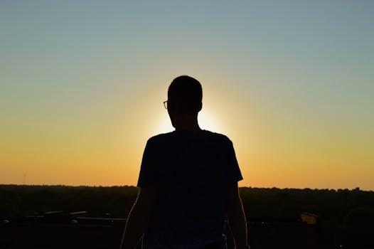 Silhouette of a person watching the sunrise over a vast landscape, creating a serene and peaceful scene.