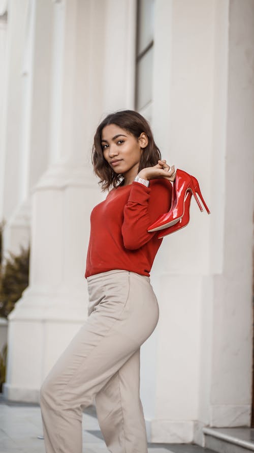 Woman in Red Long Sleeve Shirt Holding a Red High Heels Shoes
