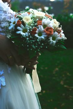 A close-up of a bridal bouquet featuring white roses and orange daisies, perfect for a wedding.