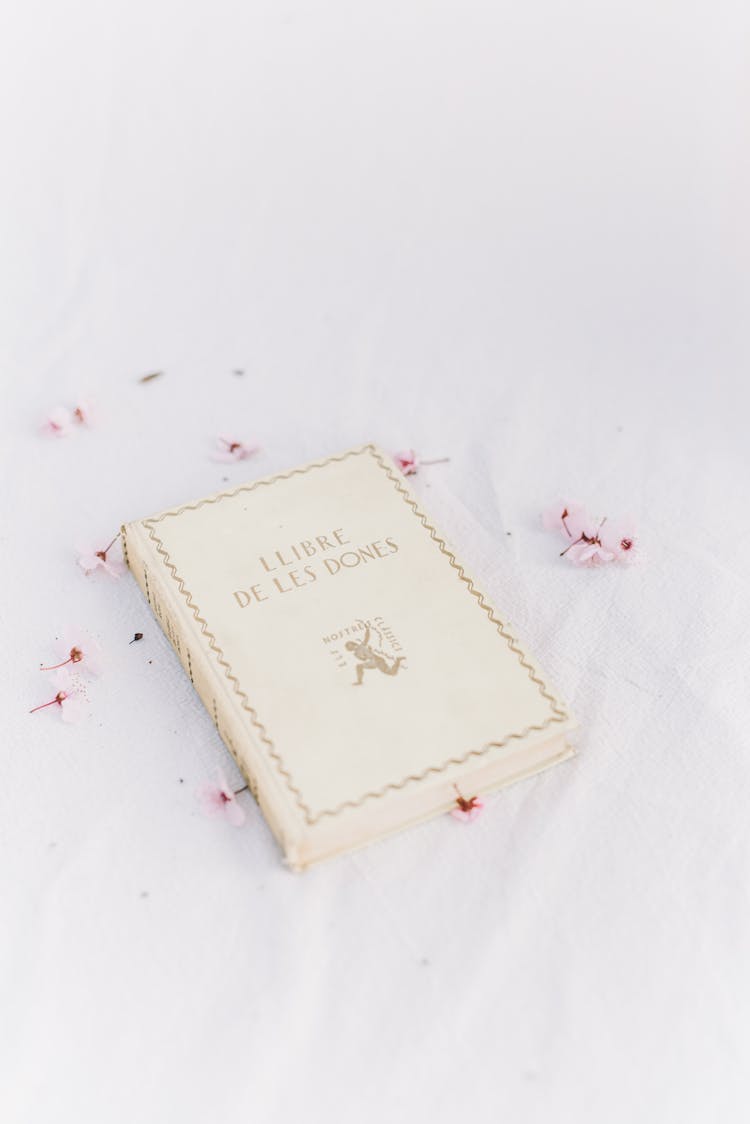 A White Women's Book On White Table With Scattered Flowers