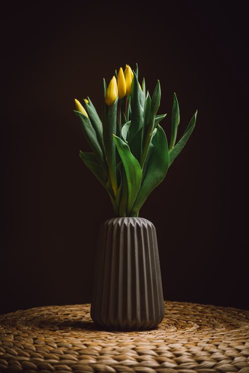 Free A beautiful arrangement of yellow tulips in a textured vase sits on a woven surface against a dark background. Stock Photo