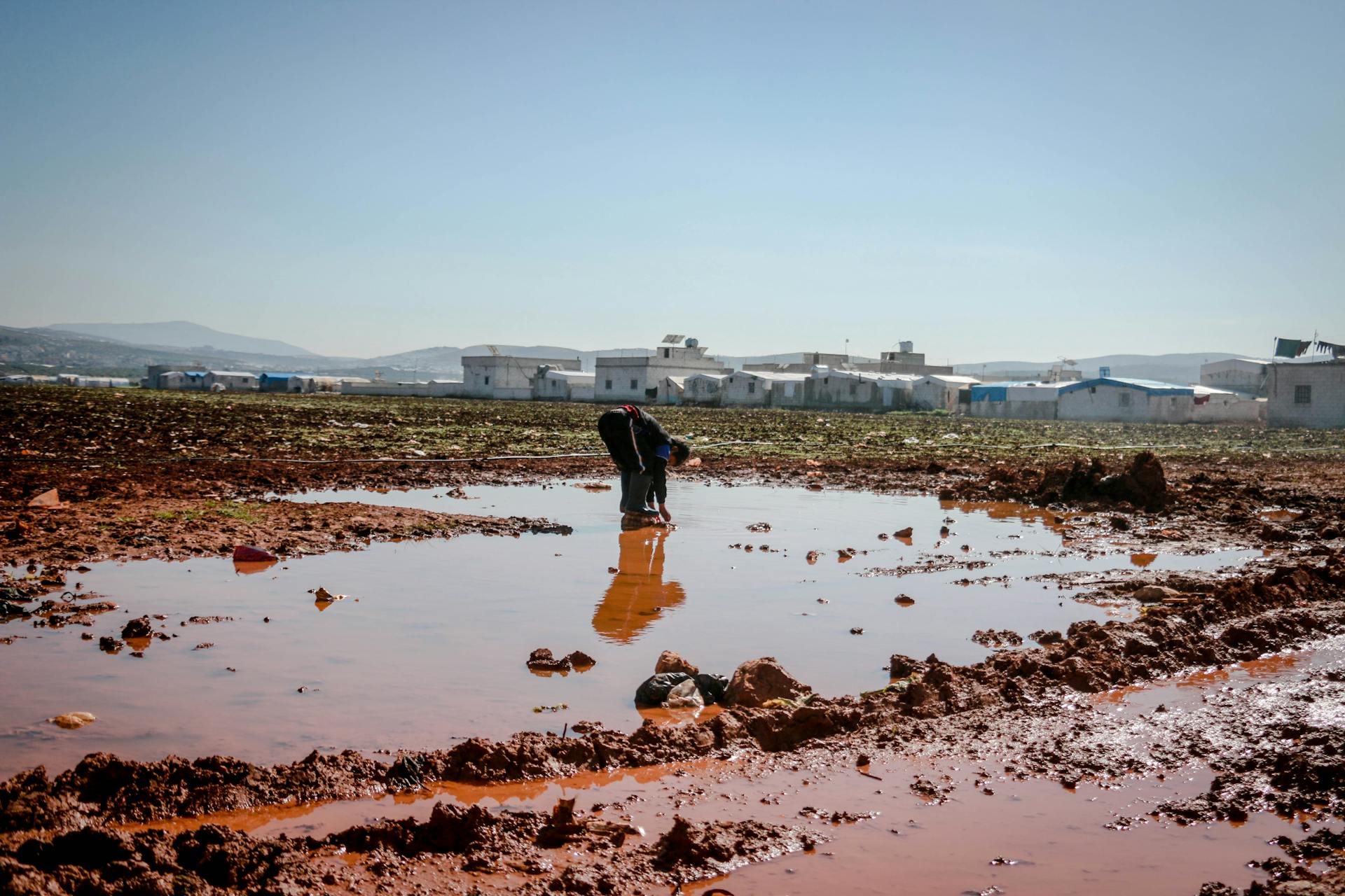 Man examines muddy water in rural Idlib, Syria after rainfall.