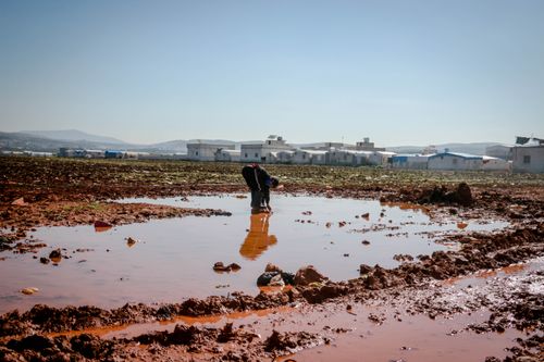 Free Side view of anonymous male washing legs with water surrounded with mud near small settlement Stock Photo