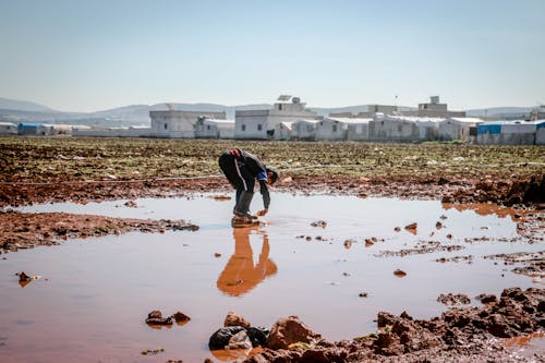 Free Full body of anonymous male pouring dirty water on legs in pond surrounded with settlement of refugee Stock Photo