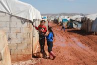 Full body of preschool and teenage ethnic girls speaking near weathered old brick residential building in poor settlement