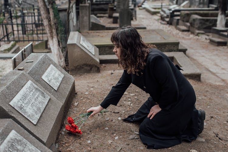 A Woman In Black Dress Offering Flowers On A Tombstone