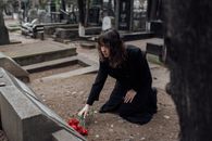 Woman In Black Coat Offering Flowers In Cemetery Grave