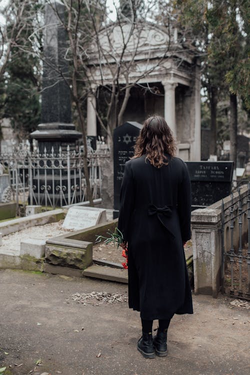 Free Woman Standing On Pathway Looking At A Grave From Afar Stock Photo