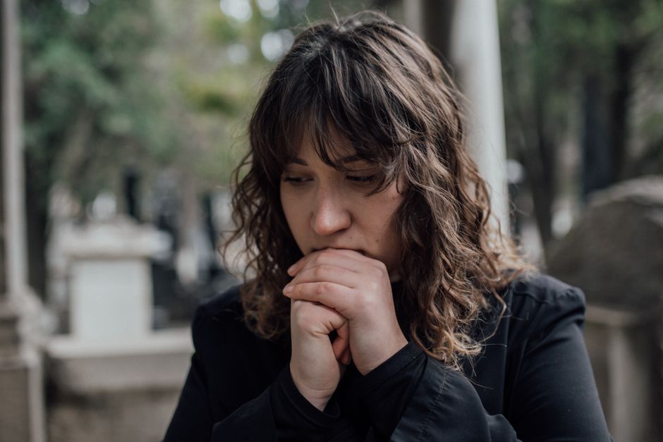Como a Meditação Pode Ajudar a Lidar com o Medo de Morrer 2 Pensive woman in black coat standing outdoors with hands together, conveying sadness.