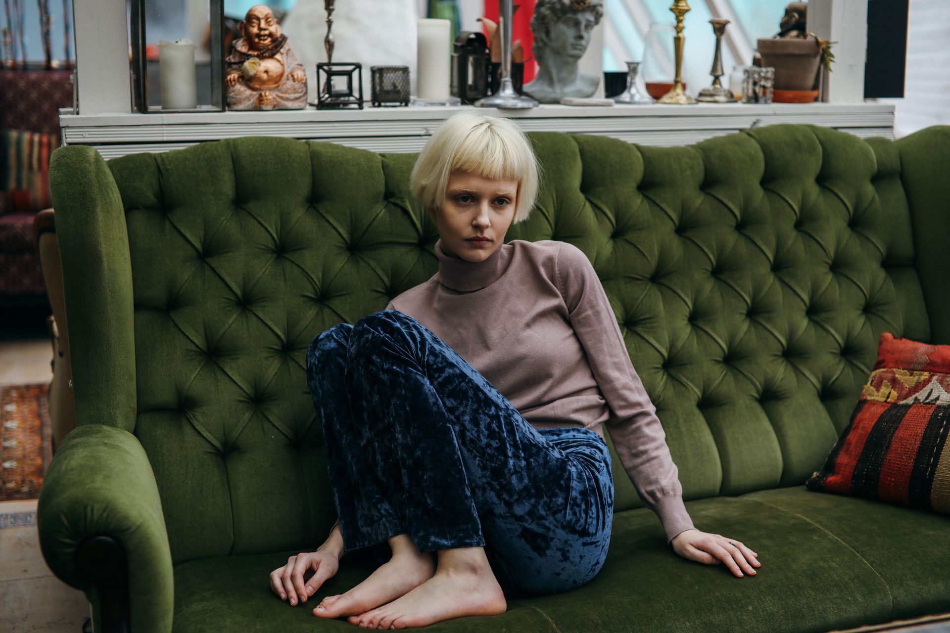 A woman with blonde short hair sits on a green sofa in a cozy, stylish room, evoking a sense of calmness.