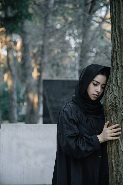 Upset woman in black outfit leaning on tree in daylight