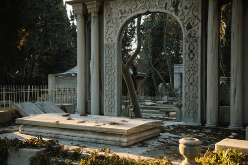 Free Old stone graves with ornamental sculptures placed in cemetery among green trees in sunny day Stock Photo