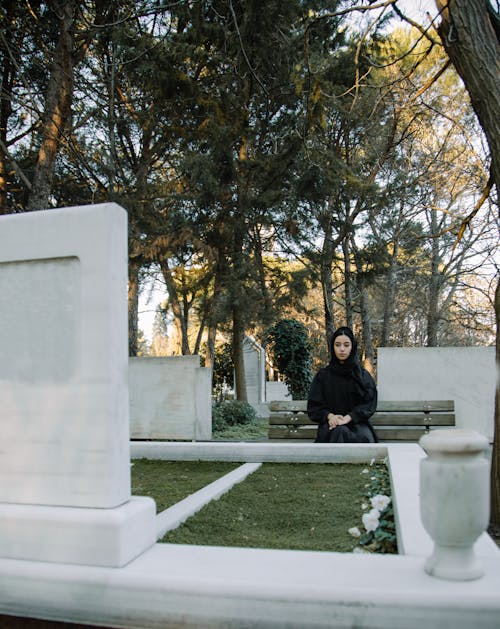 Unhappy woman on bench against gravestone in cemetery