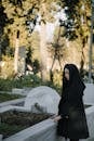 Side view of young sorrowful female in black clothes looking down against trees in graveyard