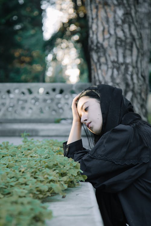 Free Hopeless woman touching head while leaning on grave Stock Photo