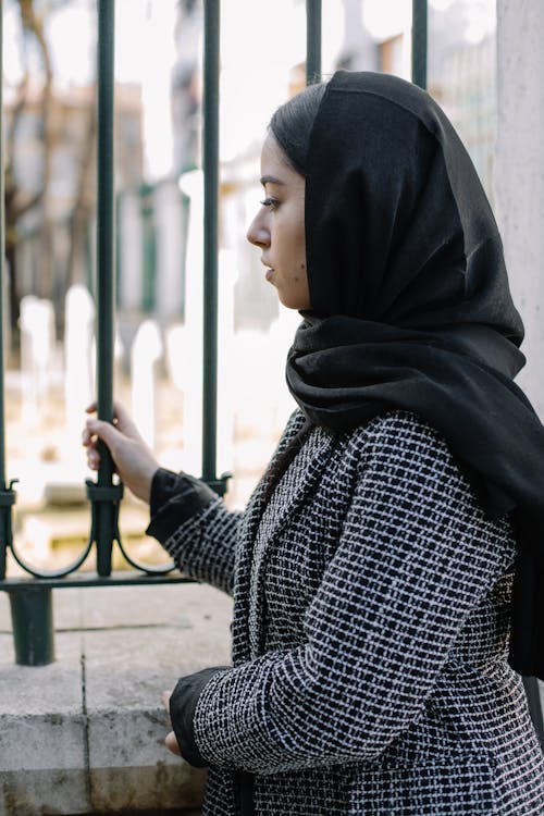 Free Melancholic woman in headscarf against fence in cemetery Stock Photo