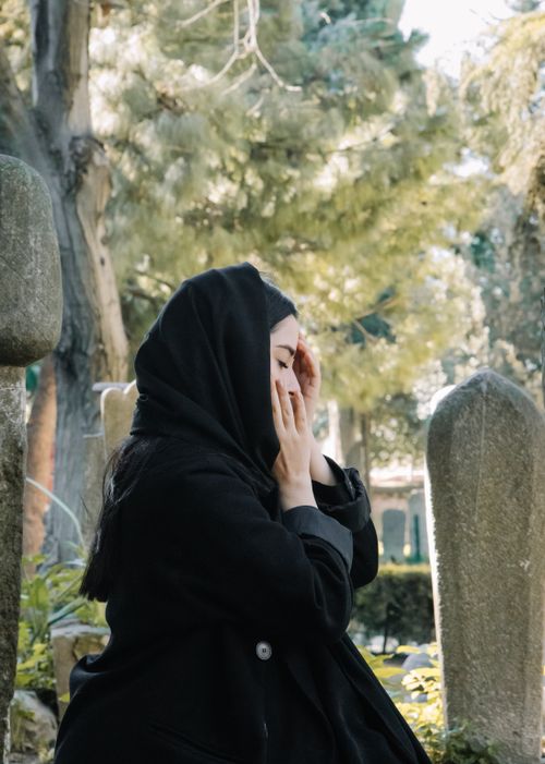Free Side view of young sorrowful female in black clothes touching face with closed eyes in graveyard Stock Photo