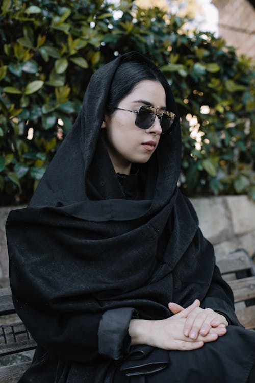 Unhappy woman in black sunglasses resting on bench outdoors
