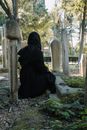 Back view of anonymous female wearing black clothes sitting near gravestone in graveyard