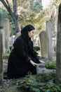Side view of female in black clothes grieving at grave for loss among stone monuments and trees
