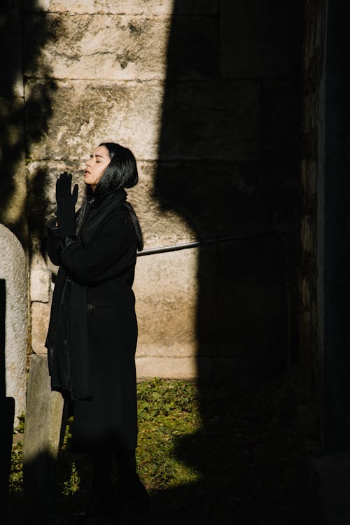 Free Side view of female in mourning black clothes and headscarf praying with closed eyes in cemetery Stock Photo